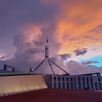 Enlighten Festival - New Parliament House, with a column of purple cloud behind the spire of Parliament House, with the rest of the sunset behind evenly split between purple, orange, and piercing blue