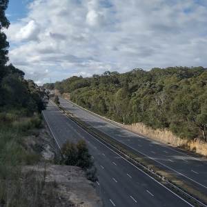 M1 Big Dipper: bottom right corner has six-lane freeway extending into distance mid-left, dense navy green trees either side, top of picture has clouds fluffy like mashed potato;