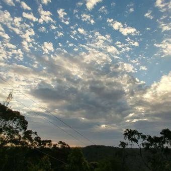 Scattered Clouds, with dark green trees fading away into the valley into much darker trees on the other side, with the sun hiding behind dotted and streak clouds causing them to appear chequered