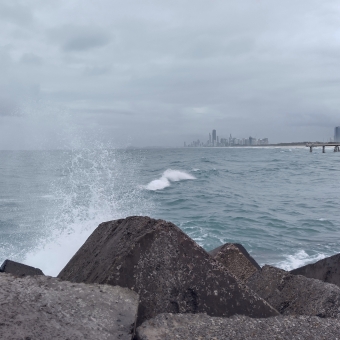 Gold Coast Splash, The Spit, Gold Coast, with a finely-misted splash from a wave on the left which splashes off the rocks below, with the greyed silhouette of the Gold Coast on the horizon across the ocean