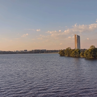 Golden Hour, National Carillon, Parkes, with the pylons of the Carollin emanating from trees on an island in the middle of Lake Burley Griffin, with clouds both hazy and looking like mashed potatoes along the horizon, with everything tinted pastel peach by the setting sun