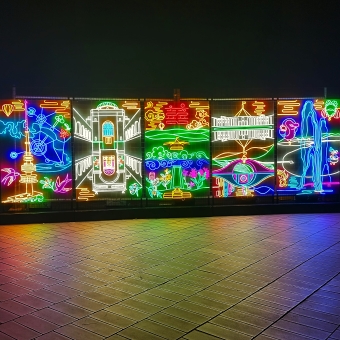 Enlighten Festival - Neon Canberran Icons, with five panels of glowing neon representing Telstra Tower and the War Memorial and Mount Ainslie and New Parliament House and Captain Cook Fountain, with the reflection of these panels on the stone ground