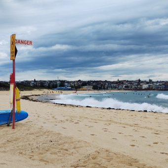Danger In The Surf, Maroubra Beach, with a lifeguard's flag with the word 'danger' on it, with waves crashing against the shore mirroring the rolling clouds in the sky