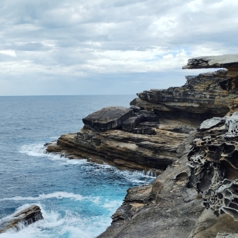 Honeycombed Cliffs, Magic Point, with rolling cliffs on the right which has patterns in the rocks caused by wind and water, with crystalline blue water on the left