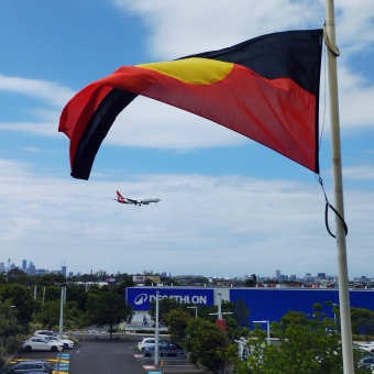 Australian Spirit, IKEA, Tempe, with an Aboriginal Flag in the foreground and a QANTAS plane in the sky against a streaky sky