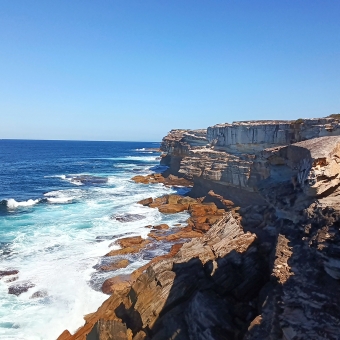 Crashing Cliffs, near The Balconies, Royal National Park, with large rolling waves crashing against tall cliffs in centre frame which extend nakedly to the right